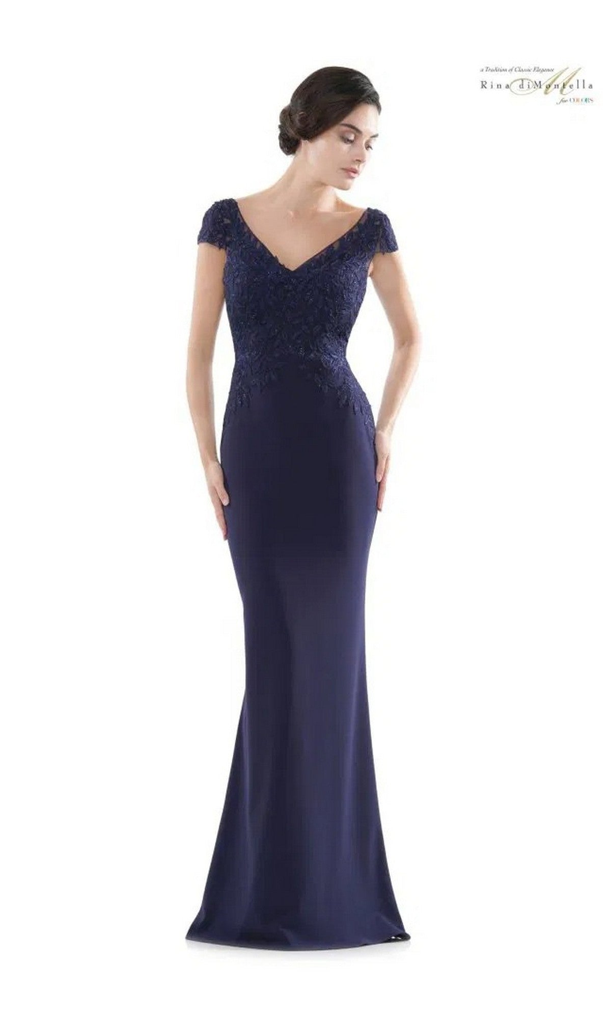 A woman wearing the Rina Di Montella RD2718, a navy long formal dress featuring short sleeves, a v-neckline, and lace detailing on the embroidered bodice with a fitted silhouette.